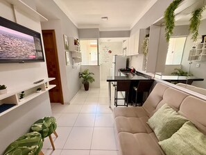 Una sala de estar moderna con un televisor de pantalla plana, un sofá y un comedor con una cocina al fondo.