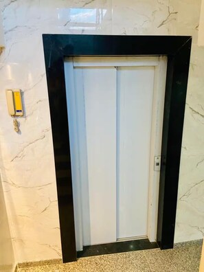A closed elevator door with a marble wall and a light switch on the wall.