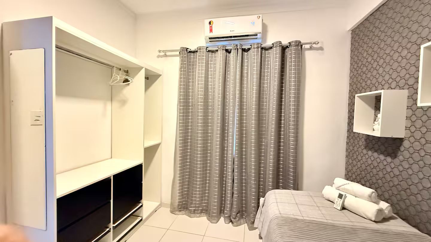 Habitación de hotel con cama, zona de ducha, armario y estante empotrado.