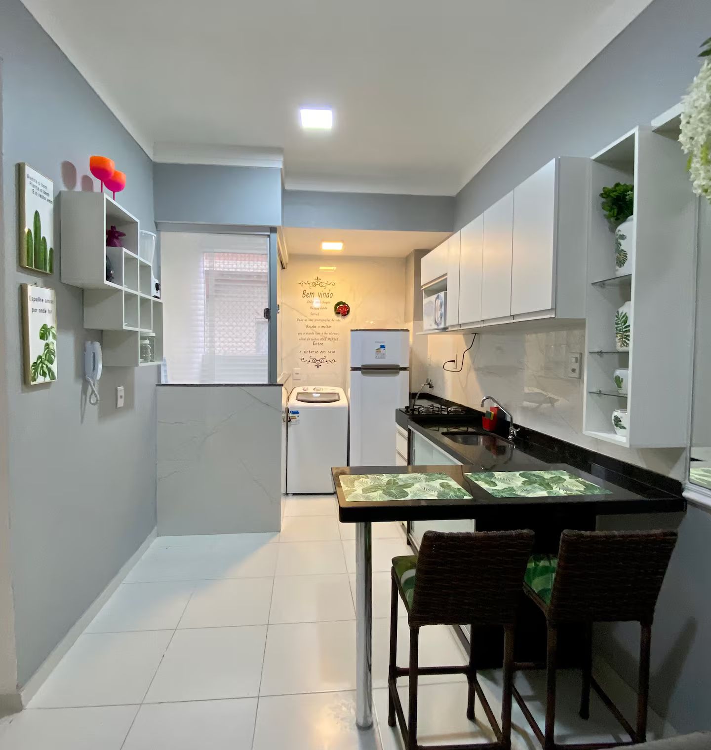 A compact kitchen with white cabinets, a refrigerator, a sink, and a dining area with two chairs.