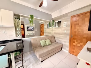 A modern kitchen with a built-in stove, a dining area with a table and chairs, a beige sofa, and a wooden door. - 204 - Cozy 2-bedroom apartment. (Belém)
