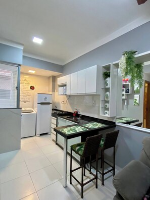 Cocina compacta con una isla central, armarios blancos y una pequeña zona de estar con dos sillas.