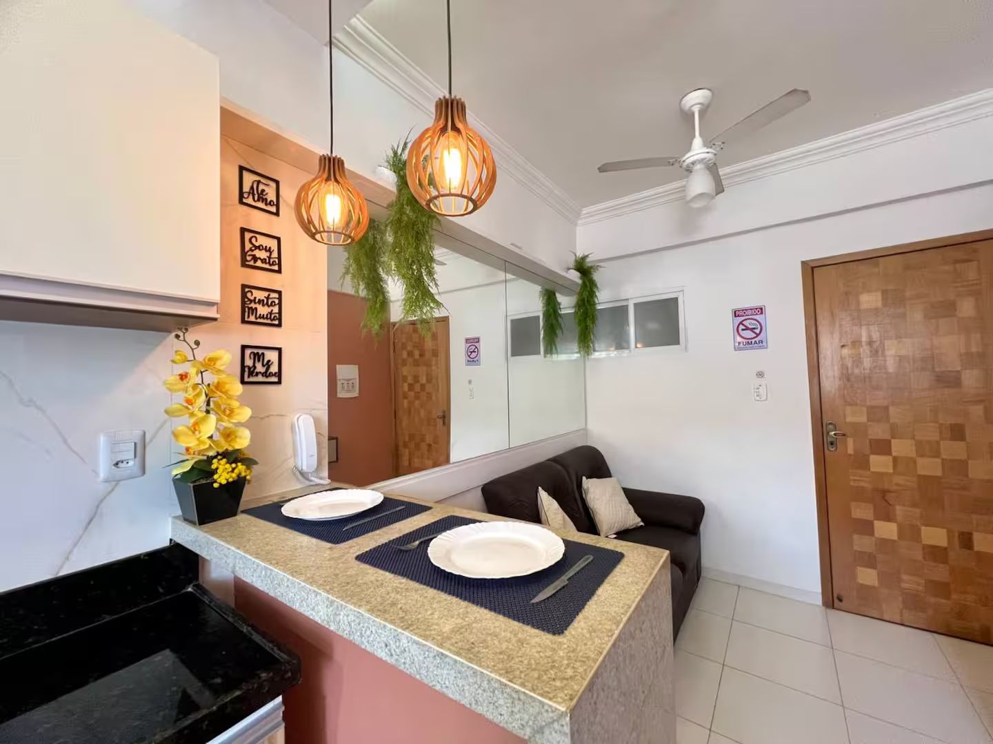 A modern kitchen with a granite countertop, two pendant lights, a ceiling fan, and a wooden door.