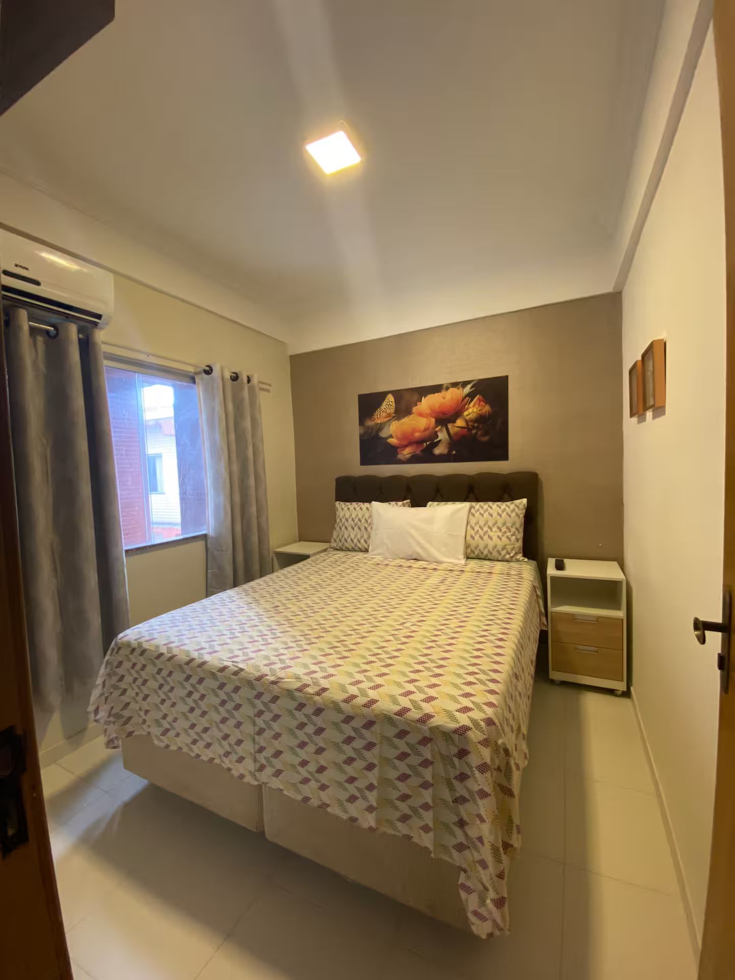 Une chambre à coucher comprenant un lit, une table de chevet, une œuvre d’art accrochée au mur et une fenêtre avec des rideaux.