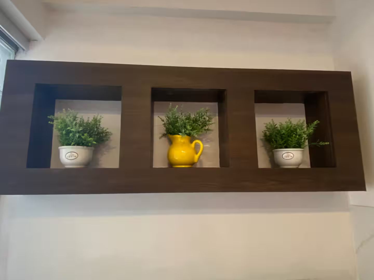 Una repisa montada en la pared con tres macetas, una de ellas un jarro amarillo.