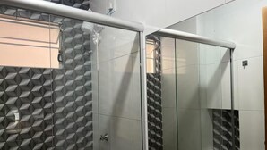 Een moderne badkamer met een wand met een geometrisch patroon, een glazen douchecabine en een vloer van witte tegels.