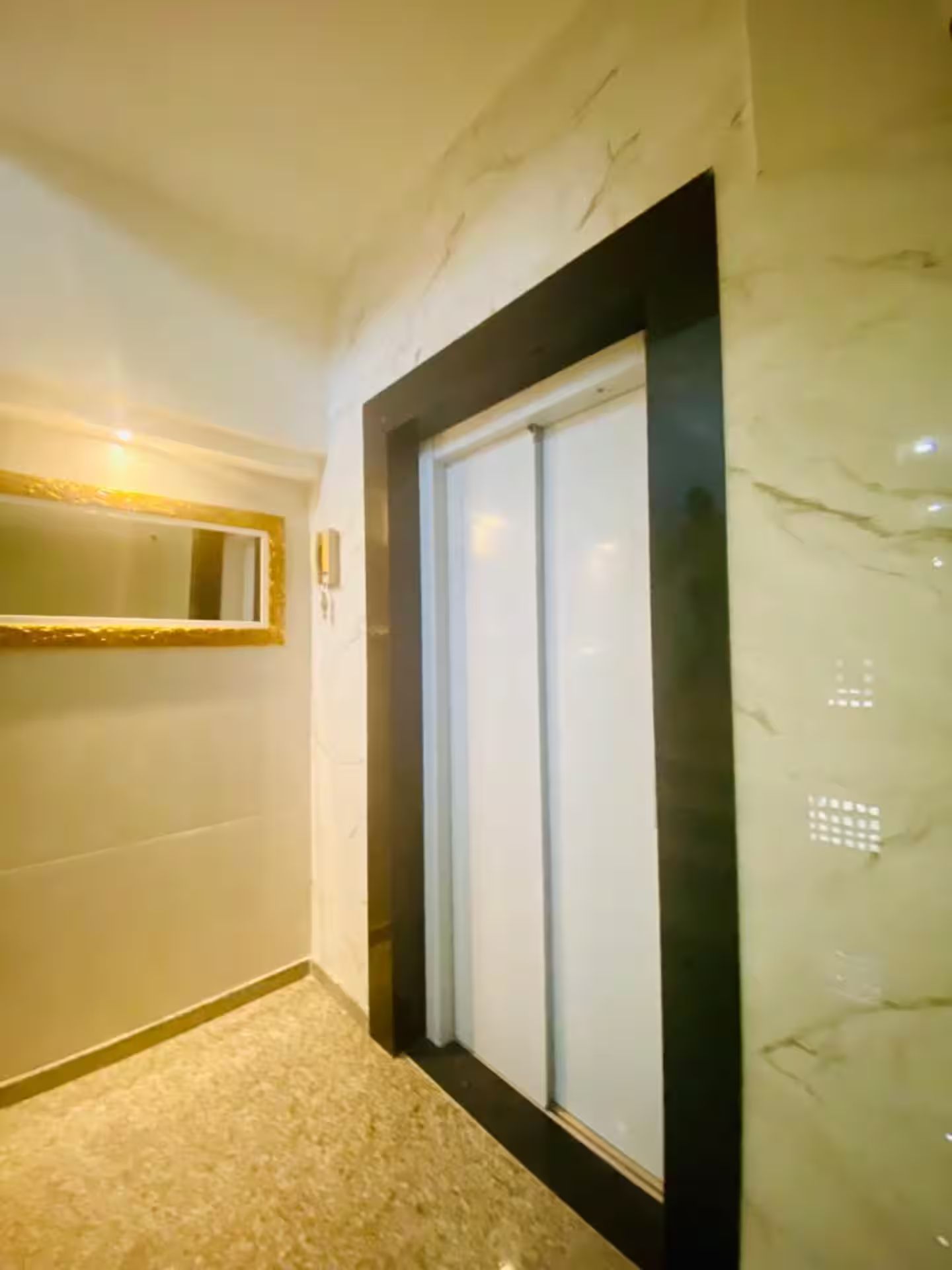 A hallway with a marble floor, a framed mirror, and a door with frosted glass.