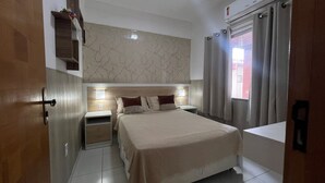 Een slaapkamer met een bed, nachtkastjes, een wandplank en een raam met gordijnen.