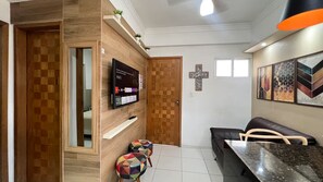 A modern living room with a flat-screen TV, a wooden wall, a black leather sofa, a dining table, and colorful stools. - Apartment 207 - 207 apartment with 2 bedrooms, beautiful. (Belém)