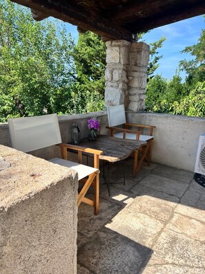 Une terrasse extérieure avec une table en pierre et deux chaises, une lanterne et un vase rempli de fleurs.