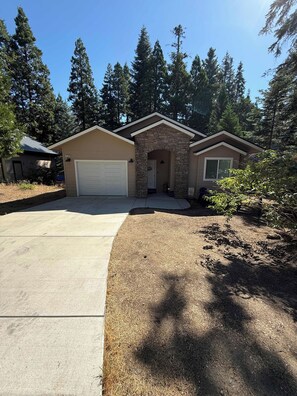 A single-story house with a stone facade, a garage, and a well-maintained lawn. - Silver Pines Modern Retreat-3BR New Build (Shaver Lake)