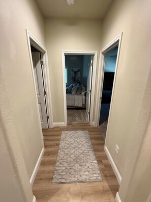 A hallway leading to a bedroom with a bed, pillows, and a rug. - Silver Pines Modern Retreat-3BR New Build (Shaver Lake)