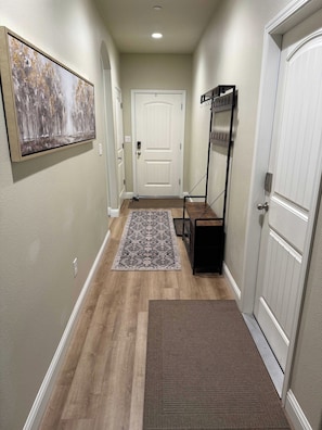 A hallway with a wooden floor, a rug, a door, and a coat rack. - Silver Pines Modern Retreat-3BR New Build (Shaver Lake)