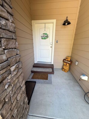 A house entrance with a stone wall, a white door with a welcome sign, a wooden bear statue, and a doormat. - Silver Pines Modern Retreat-3BR New Build (Shaver Lake)