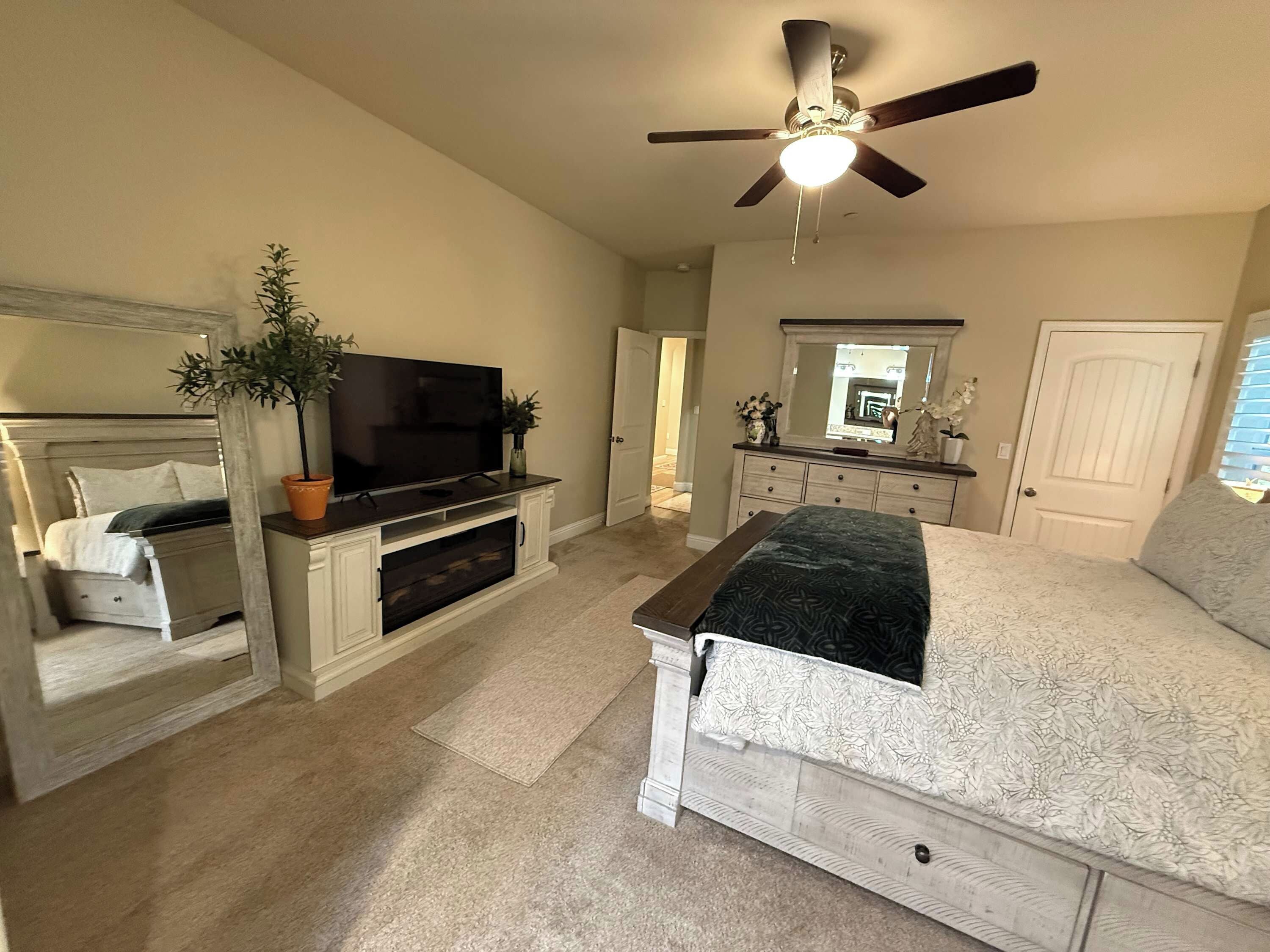 A bedroom with a bed, a TV, a ceiling fan, a dresser, and a mirror.