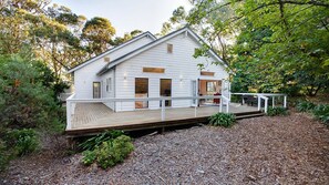 A white two-story house with a wooden deck and a small outdoor seating area. - White Cottage - Your Private Blue Mountains Escape (WENTWORTH FALLS)