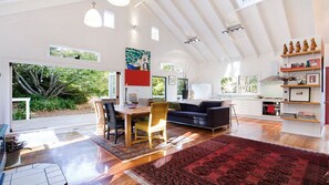 A spacious living area with a dining table, sofa, and kitchen in the background. - White Cottage - Your Private Blue Mountains Escape (WENTWORTH FALLS)
