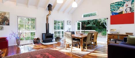 Een ruime woonkamer met een groot raam, een open haard, een eettafel met stoelen, en een rood vloerkleed.
