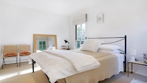 Ein Schlafzimmer mit Bett, Sessel, Nachttisch, Fenster und Spiegel.