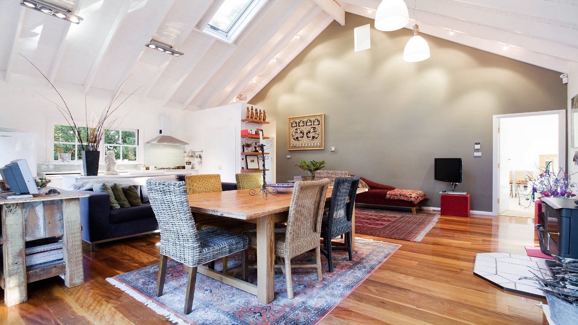 Un loft spacieux avec de hauts plafonds, un coin repas avec une table en bois et des chaises en osier, un salon avec un canapé rouge et une cuisine avec des meubles blancs.