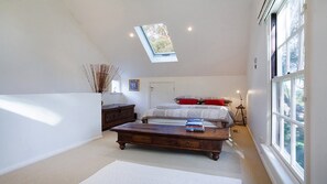 A bedroom with a skylight, a bed with pillows, a bedside table, a dresser, and a window. - White Cottage - Your Private Blue Mountains Escape (WENTWORTH FALLS)