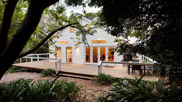 A modern house with a deck, surrounded by lush greenery.