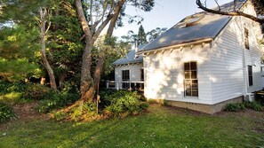 A white wooden house with a gabled roof, surrounded by trees and a grassy yard.