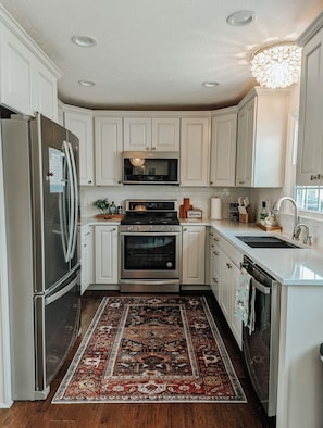 A kitchen with white cabinetry, stainless steel appliances, a patterned rug, and a chandelier. - Spacious 4-bedroom house in peaceful neighborhood. (Jerome)