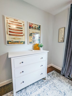 A room with a white dresser, a framed poster of canoes, a camping-themed poster, and a small plant on the dresser. - Spacious 4-bedroom house in peaceful neighborhood. (Jerome)