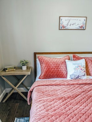 A bedroom with a bed, a bedside table, a small potted plant, and a wall sign. - Spacious 4-bedroom house in peaceful neighborhood. (Jerome)