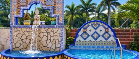 A pool area with a fountain, tiled walls, and a statue.