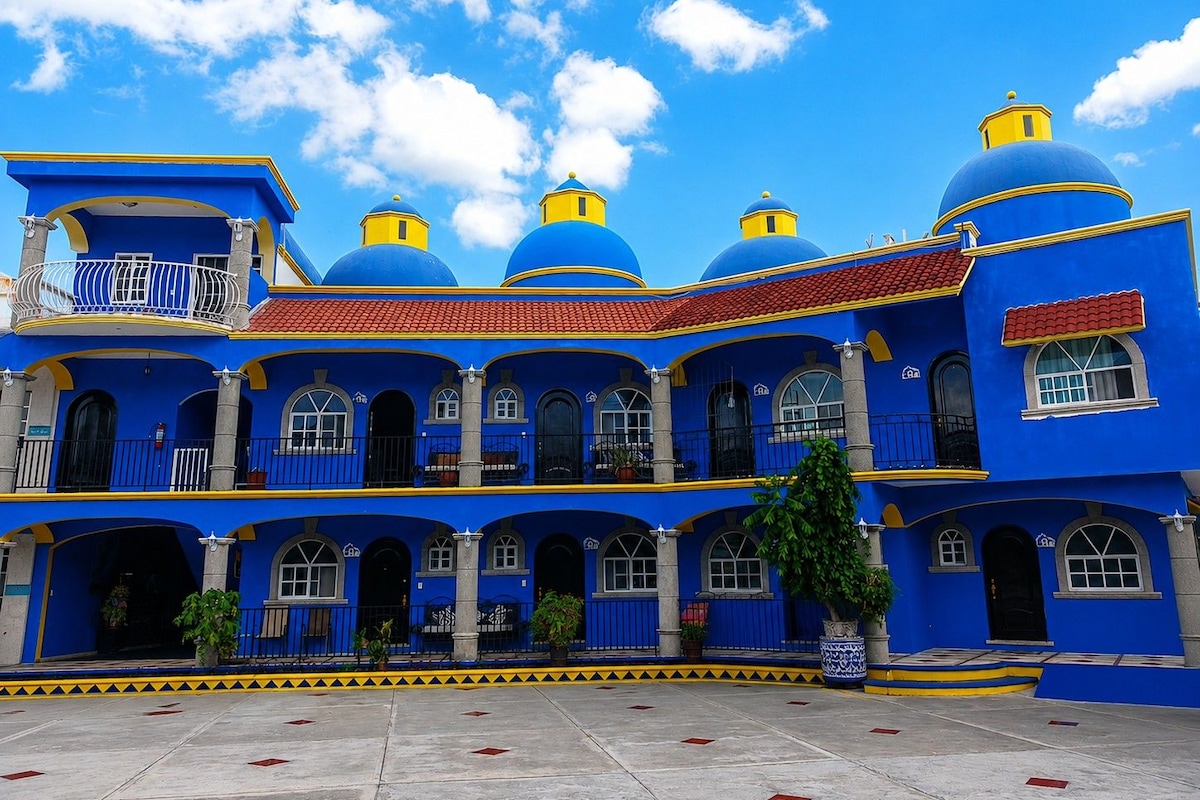 A building with multiple blue domes and yellow accents, featuring a courtyard with a tiled floor and potted plants.