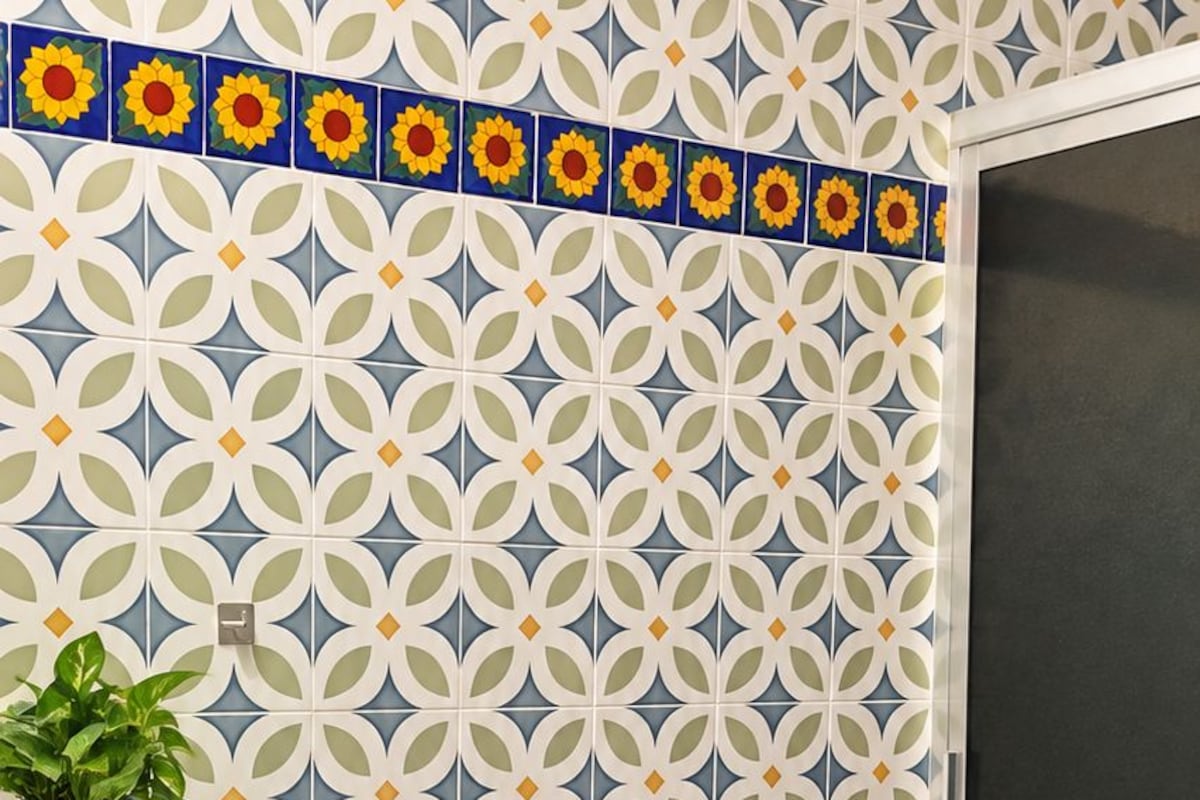 A bathroom with a patterned tile wall, a toilet, a sink with a decorative cover, and a potted plant.