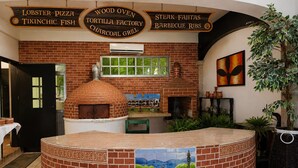 Interior de restaurante con pared de ladrillo, horno de pizza y un mural.