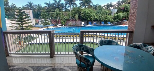 A balcony with a view of a swimming pool, surrounded by greenery and palm trees.