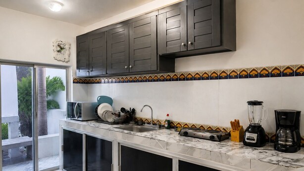 Una cocina con armarios oscuros, salpicadero de azulejos, un fregadero, una estufa, una licuadora y una cafetera.