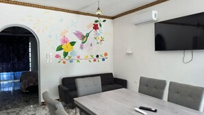Una sala de estar moderna con comedor, televisor montado en la pared y un mural decorativo.