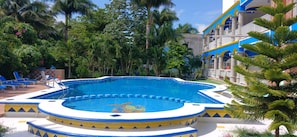 A swimming pool with a blue and yellow tiled edge, surrounded by palm trees and a building with blue and yellow accents. - Cúpulas Blue Wellness Residence (Cozumel)