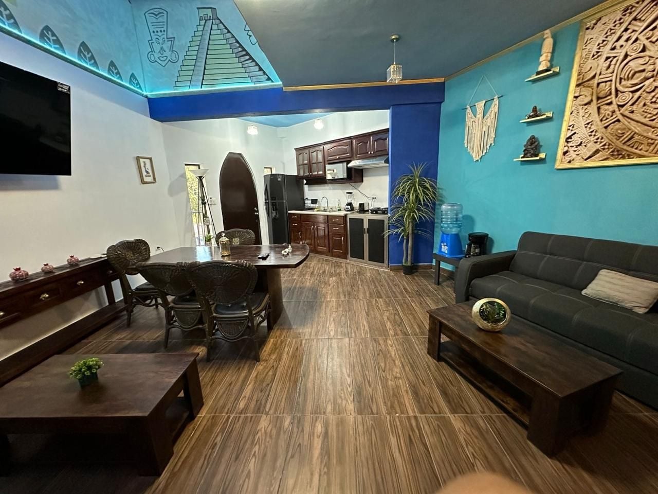Sala de estar com sofá, mesa de centro, mesa de jantar com cadeiras e cozinha ao fundo.