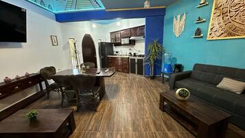 Sala de estar com sofá, mesa de centro, mesa de jantar com cadeiras e cozinha ao fundo.