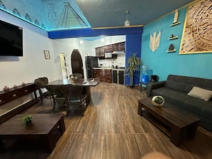 Una sala de estar con sofá, mesa de centro, mesa de comedor con sillas y una cocina al fondo.