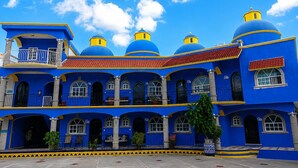 Un edificio con cúpulas azules y detalles en amarillo, que presenta un patio con suelo de mosaicos y plantas en macetas.