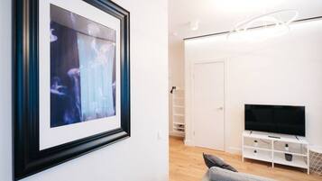Un salon moderne avec un tableau encadré, un canapé gris, un meuble de télévision blanc avec un téléviseur, et une porte blanche en arrière-plan.