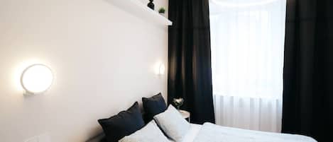A modern bedroom with a bed, pillows, a bedside table, and a wall-mounted light fixture.