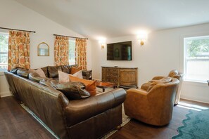 A living room with a brown leather sofa, a wooden cabinet, and a television mounted on the wall. - Pecan Manor Off Main - Historic Downtown Franklin (Franklin)