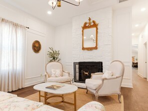 A living room with a fireplace, two armchairs, a coffee table, and a white-framed mirror on the wall. - Pecan Manor Off Main - Historic Downtown Franklin (Franklin)