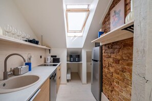 A compact kitchen with a skylight, a brick accent wall, and modern appliances. - Stylish Scandi-Loft Gem with Exposed Brick & Beams (Riga)