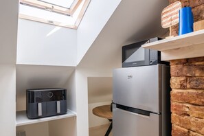A compact kitchen with a built-in microwave, a refrigerator, and a small seating area. - Stylish Scandi-Loft Gem with Exposed Brick & Beams (Riga)