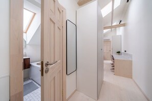 A modern interior with a wooden door, a white wall, and a view into a bathroom with a white sink and a small plant. - Stylish Scandi-Loft Gem with Exposed Brick & Beams (Riga)