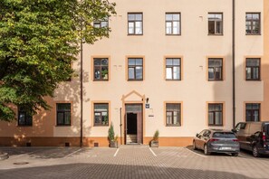 A multi-story building with a beige facade, a central entrance with a door, and a parking area with two cars. - Stylish Scandi-Loft Gem with Exposed Brick & Beams (Riga)